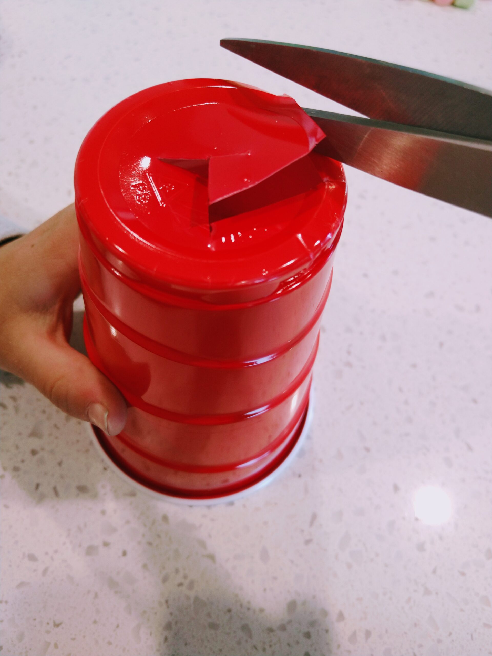 Hands using scissors to cut out the bottom of a cup.